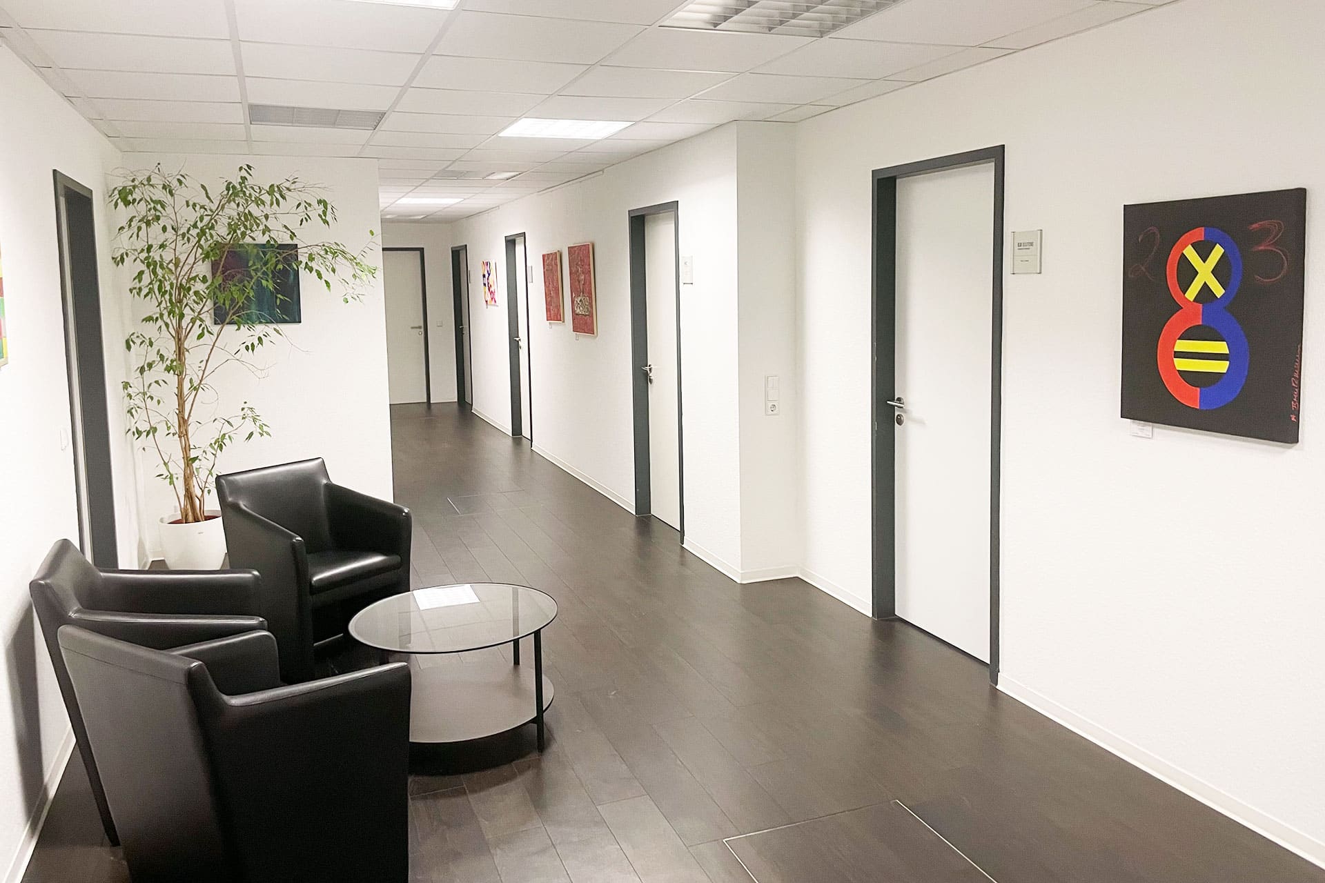 Moderner Büroflur mit Sitzbereich, Kunstwerken an den Wänden und Zugang zu mehreren Büroräumen
