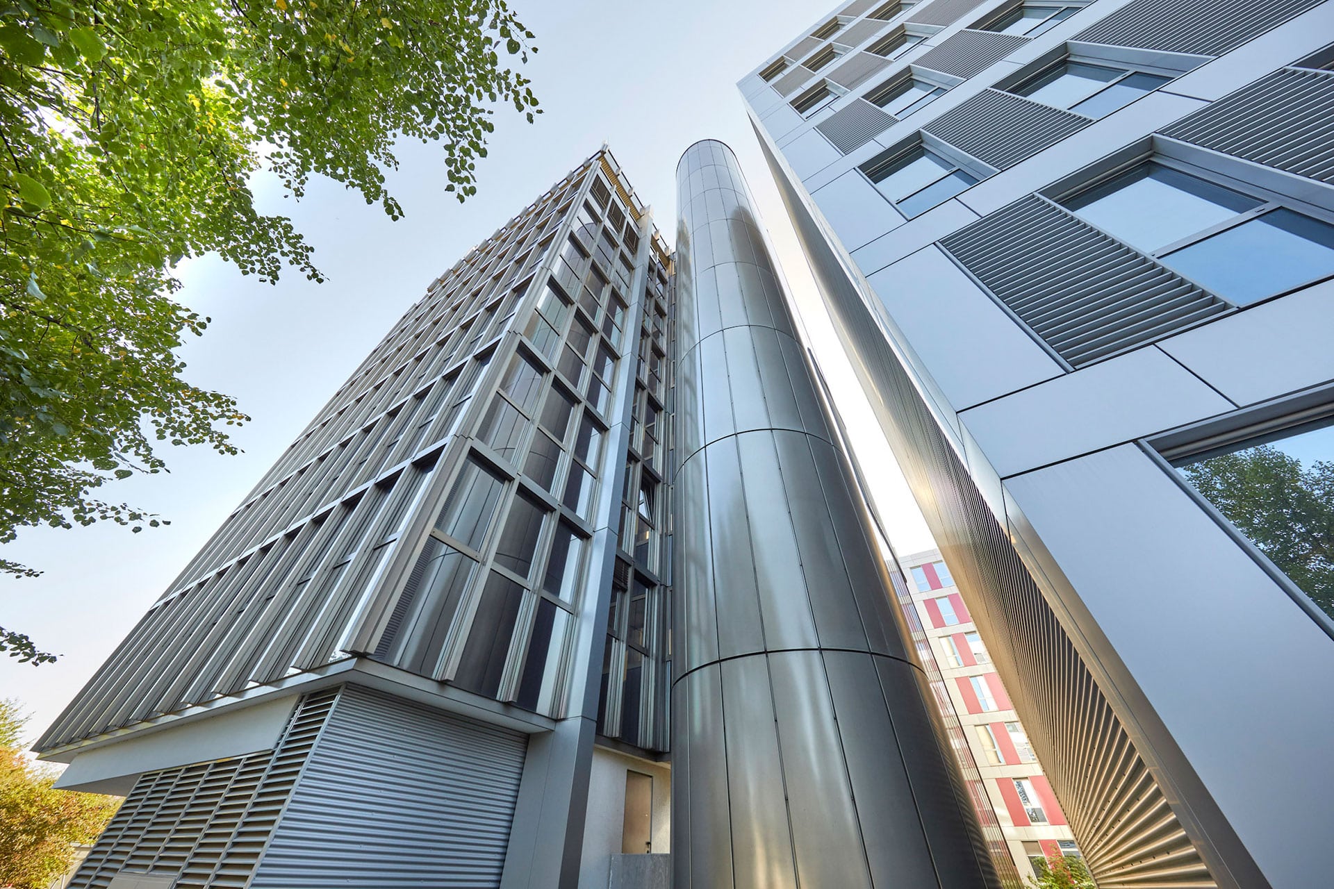 Moderne Bürogebäude-Architektur mit Glasfassade, Metallverkleidung und zentralem Aufzugsschacht in urbaner Lage